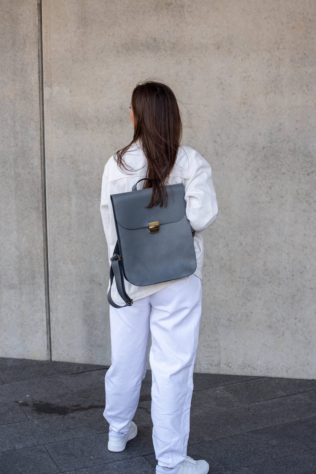 4. Women's grey Zelma Kraft leather saddle backpack worn on back, shown from behind in lifestyle setting