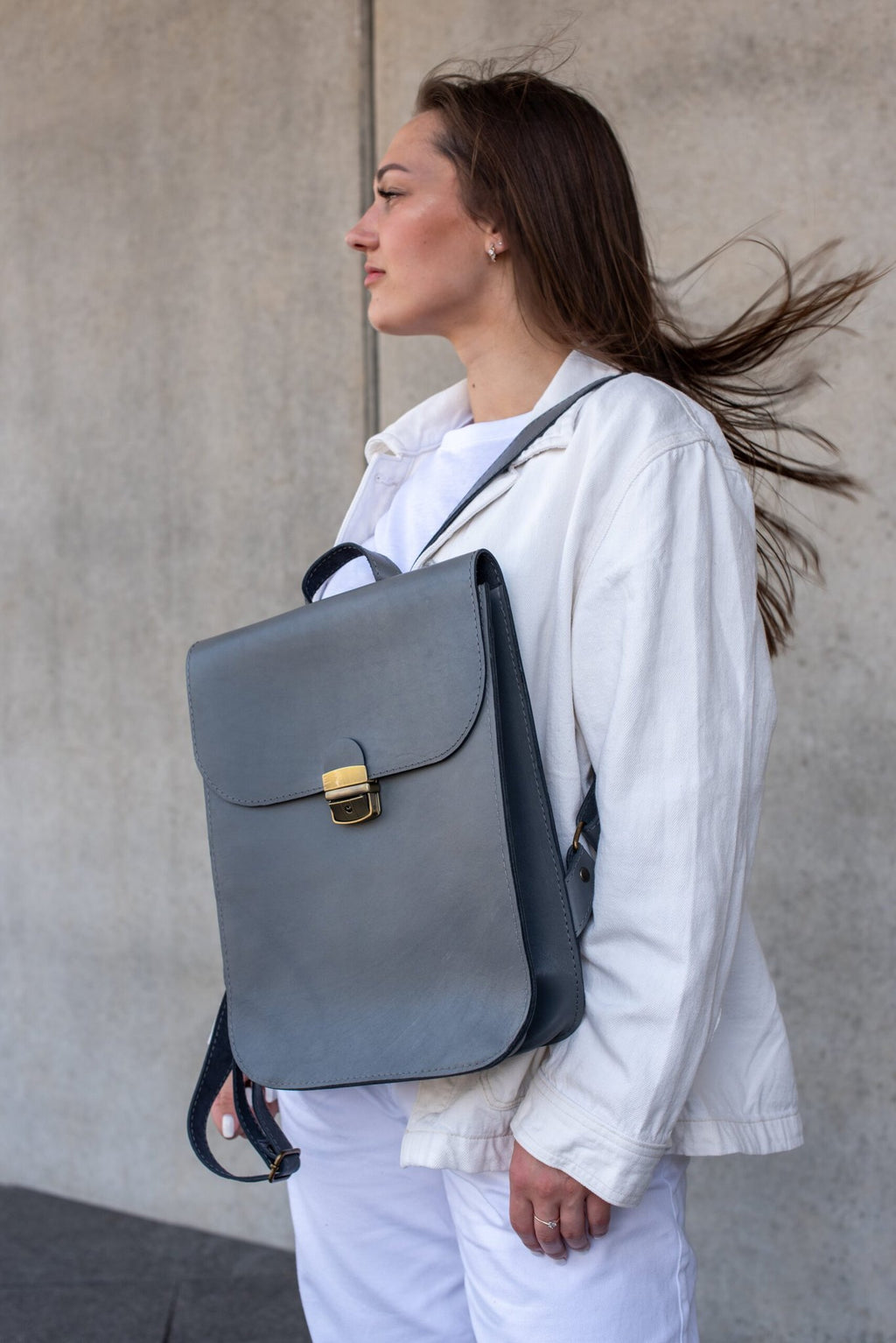6. Women's grey Zelma Kraft leather saddle backpack worn over shoulder, shown in lifestyle setting