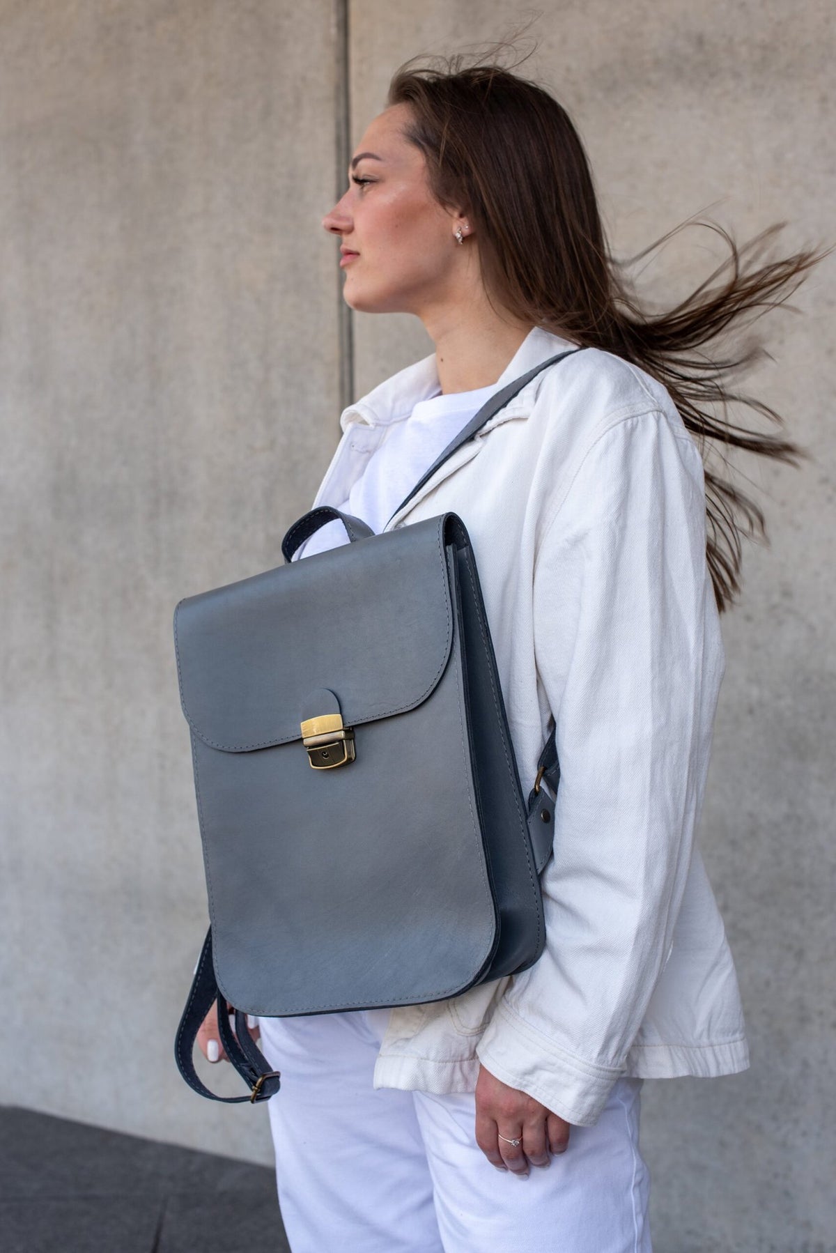 6. Women's grey Zelma Kraft leather saddle backpack worn over shoulder, shown in lifestyle setting