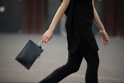 4. Woman walking with PYKOK Clutch Nina, emphasizing elegant black leather and metal ring handle in motion
