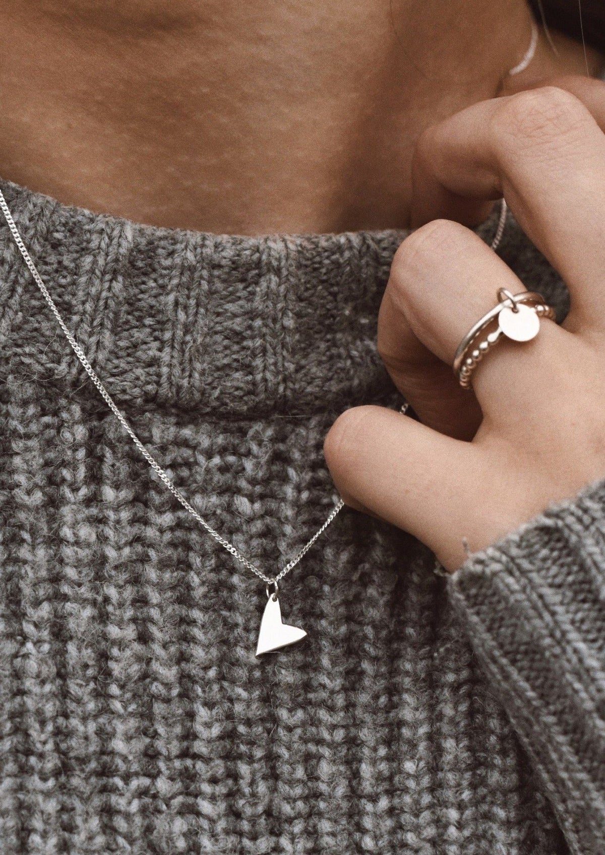 3. Woman wearing NO MORE Love Necklace in silver with heart pendant, paired with a grey knit sweater
