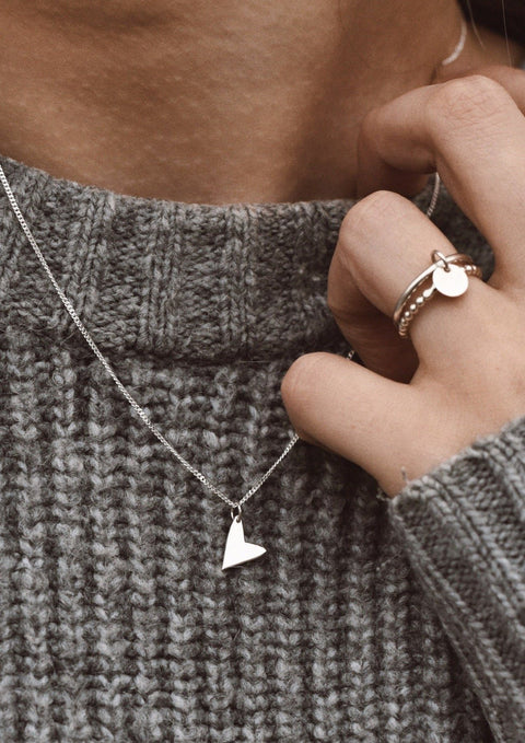 3. Woman wearing NO MORE Love Necklace in silver with heart pendant, paired with a grey knit sweater