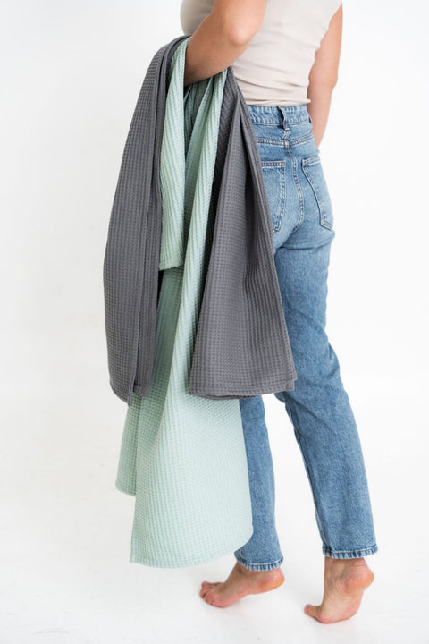 1. Woman holding sage green and grey waffle cotton towels, wearing jeans and a beige top
