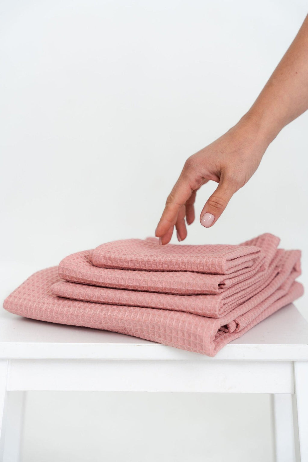 2. Hand reaching for a stack of folded peach waffle cotton towels on a white surface
