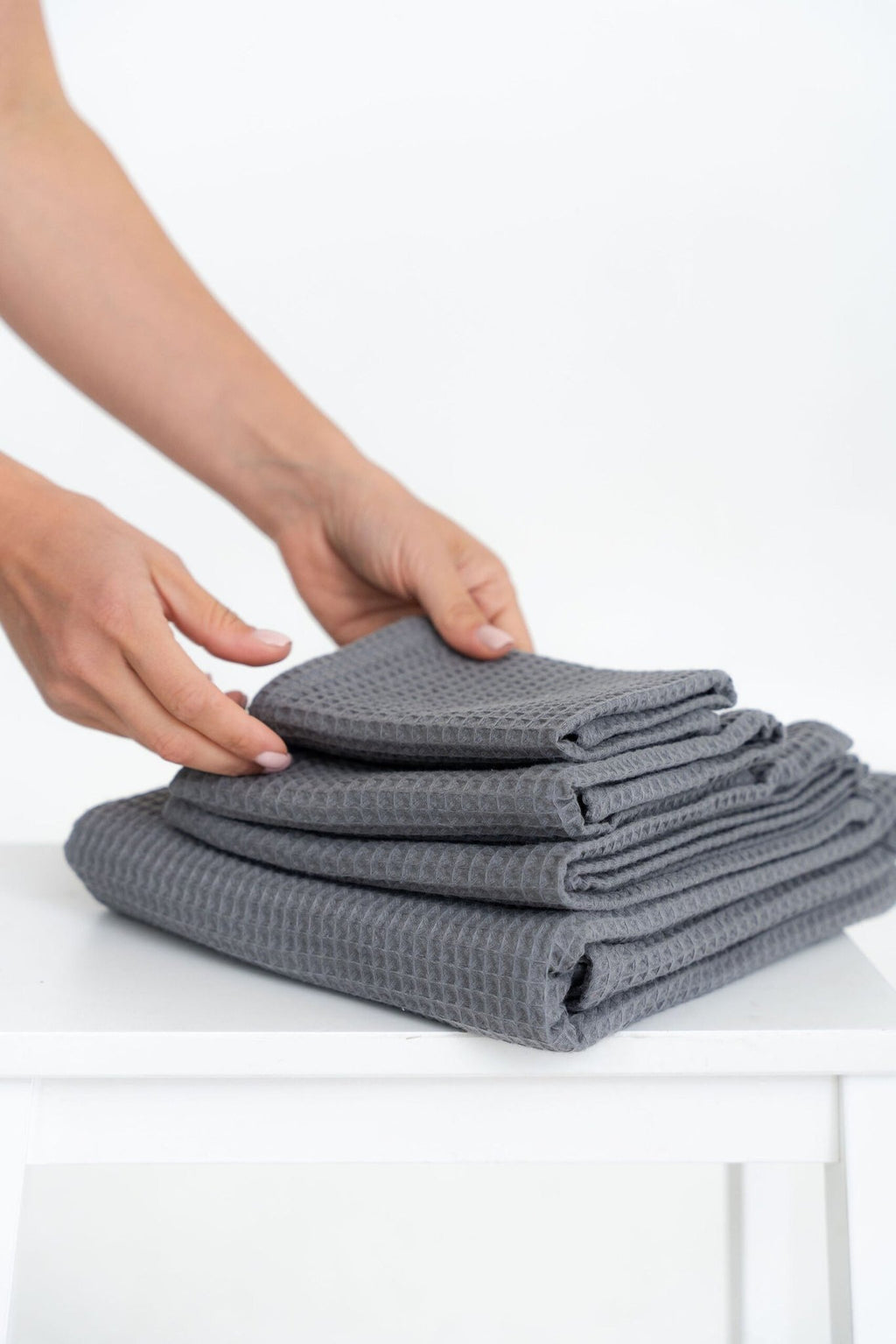 5. Hands arranging a stack of folded gray waffle cotton towels on a white surface