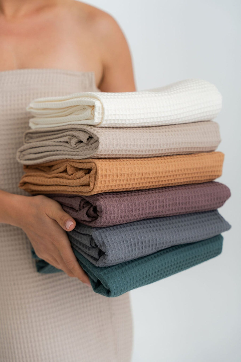 4. Stack of spa wrap towels in various colors held by woman, showing texture and color variety