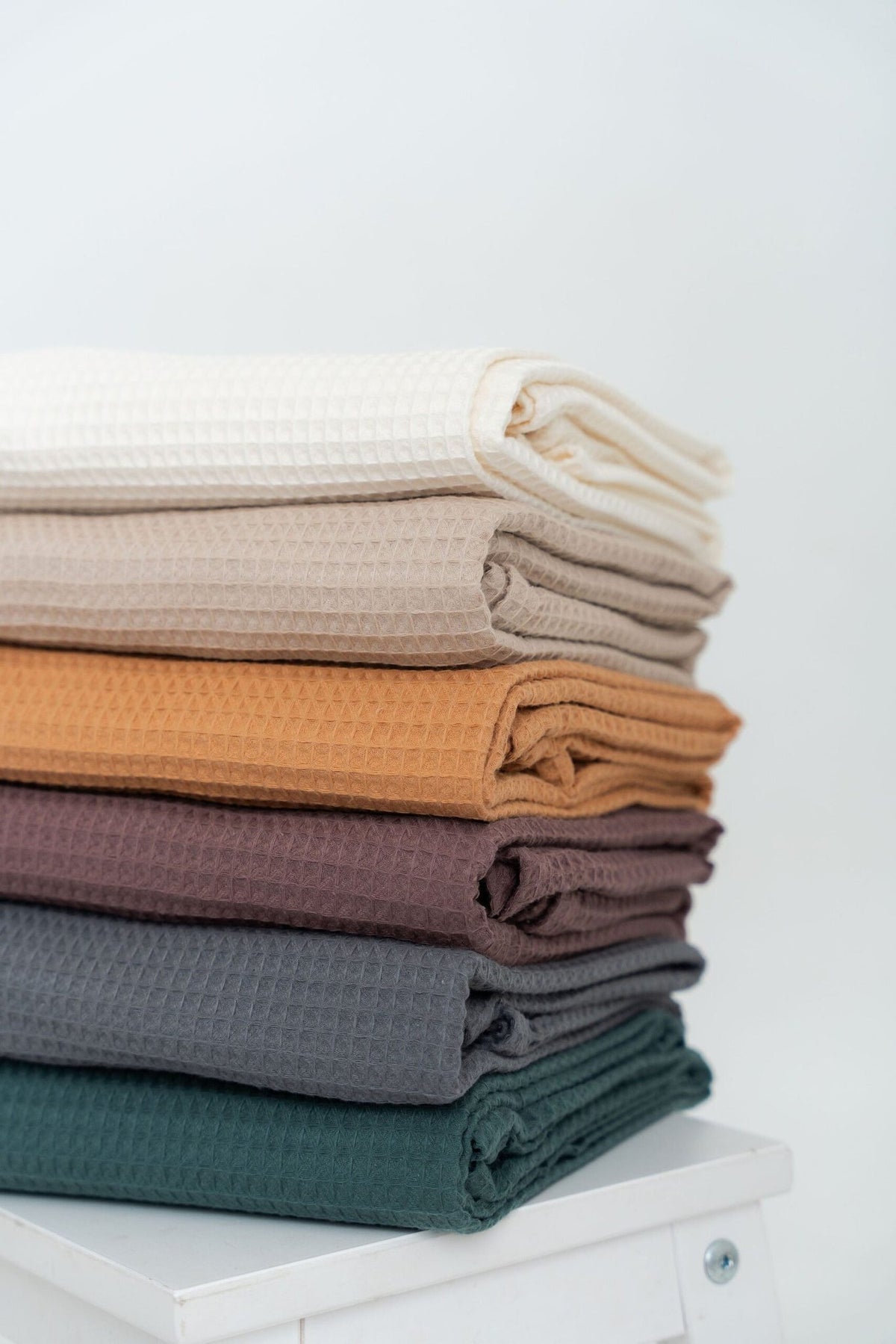 4. Flat lay of folded cotton hair towels in various colors including cream, beige, caramel, plum, gray, and petrol