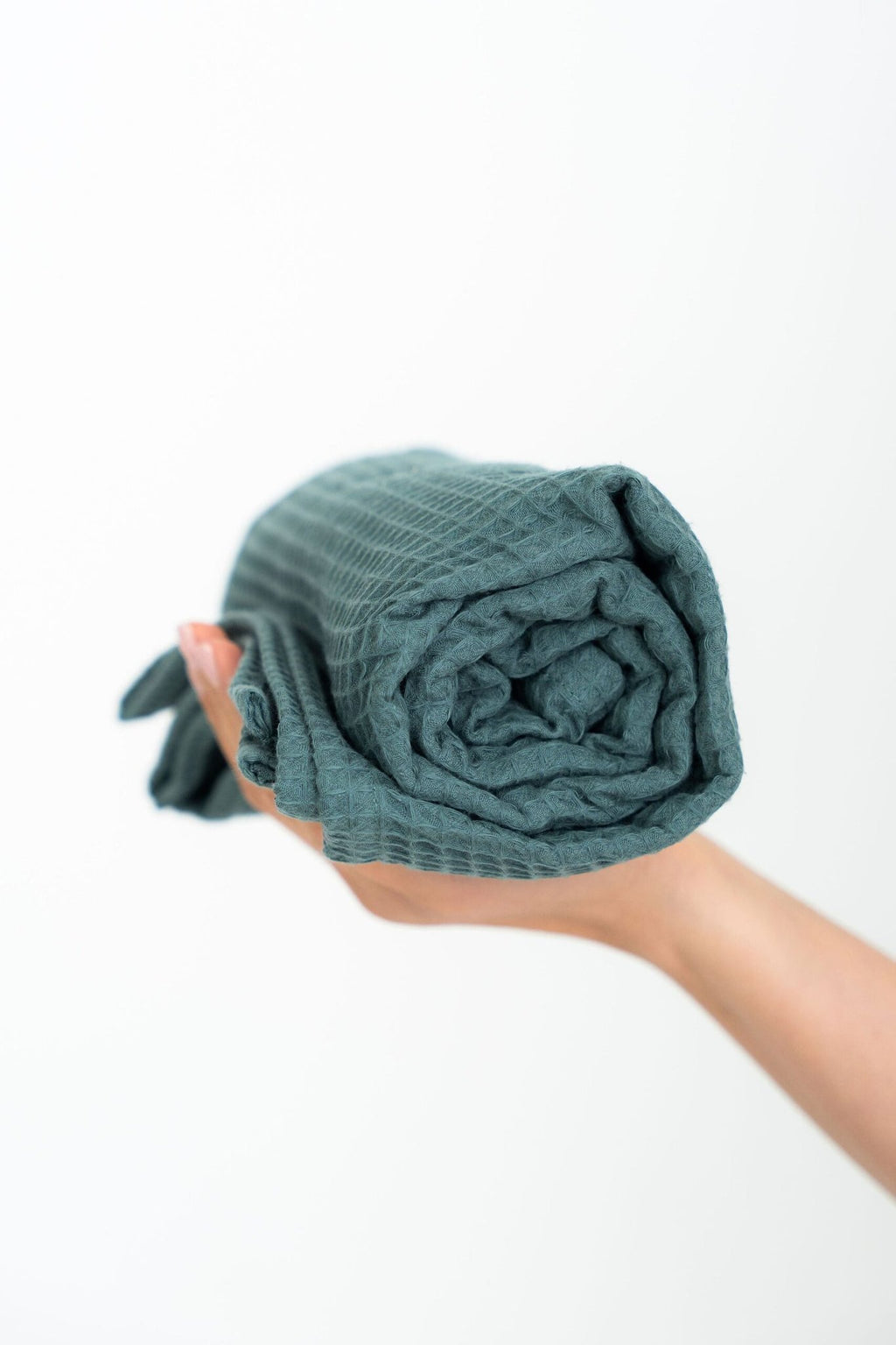 2. Rolled petrol organic waffle cotton towel held in hand against a white background