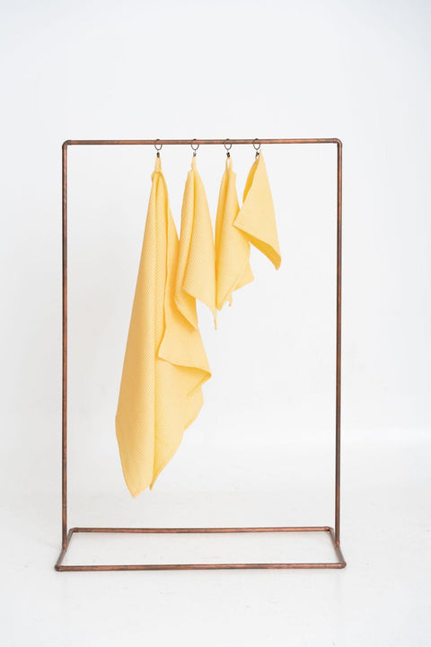 2. Full view of four yellow organic waffle cotton towels on a copper stand, highlighting their lightweight and versatile design
