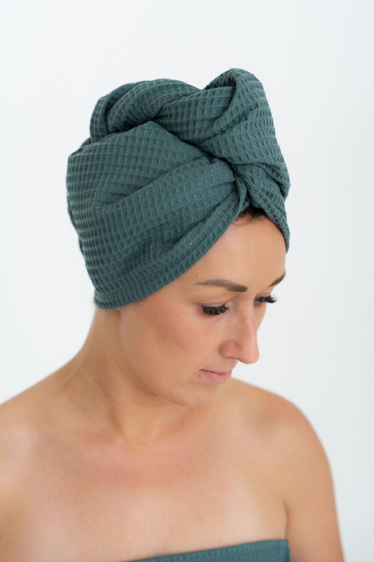 1. Woman wearing petrol green cotton hair towel with button closure, shown in profile against a white background