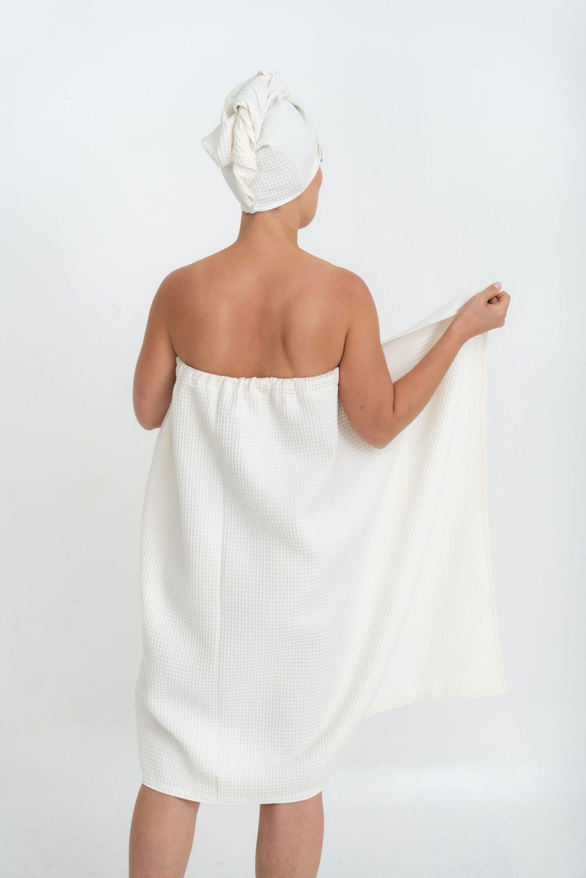 1. Woman in white spa wrap towel and head wrap, shown from back, highlighting elastic band, on white background