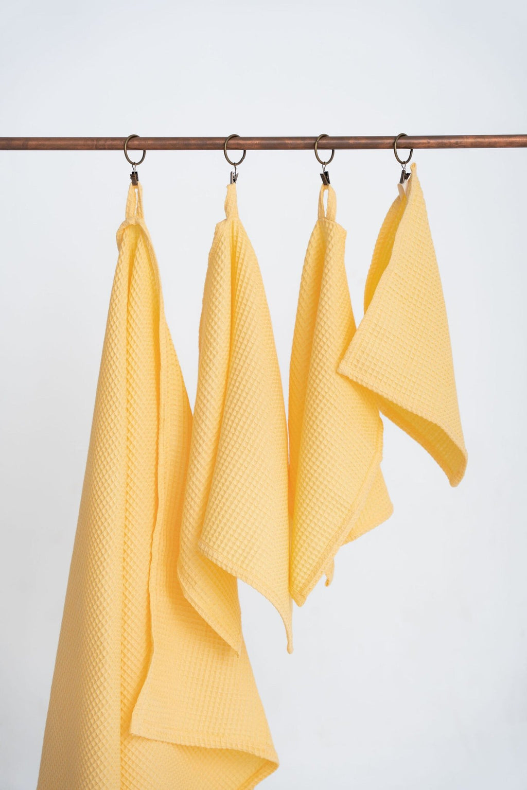 1. Set of four yellow organic waffle cotton towels hanging on a copper rod, showcasing different sizes with hanging loops