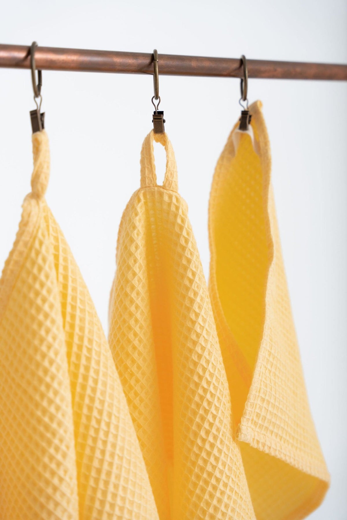 4. Close-up of yellow organic waffle cotton towels on a copper rod, showing texture and hanging loops