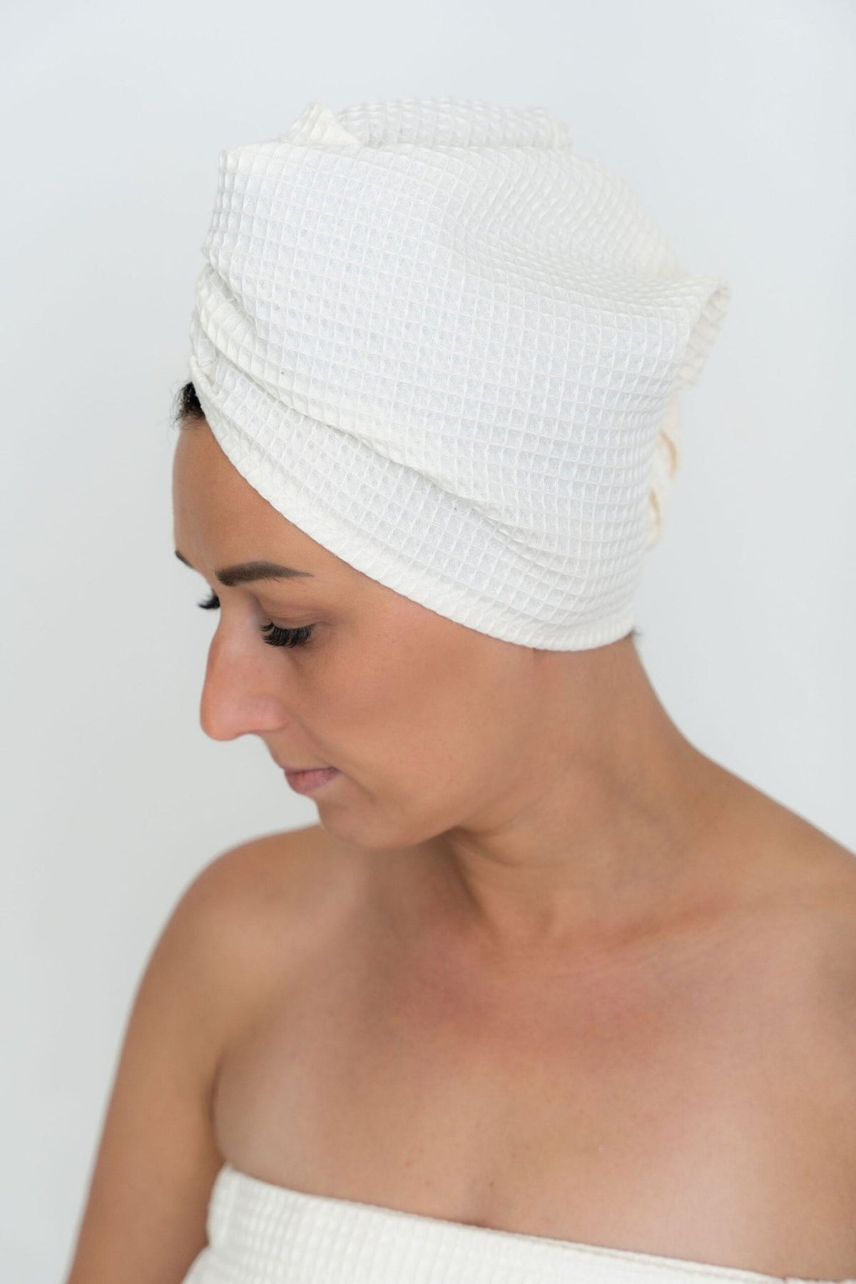 1. Woman wearing cream cotton hair towel with button closure, shown in profile against a white background