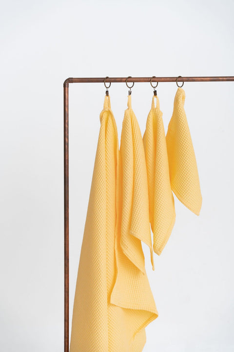 3. Yellow organic waffle cotton towels in various sizes hanging on a copper rod, emphasizing texture and absorbency