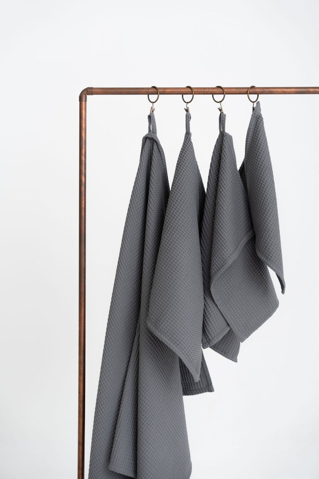 4. Four gray waffle cotton towels hanging on a copper rack in a studio setting