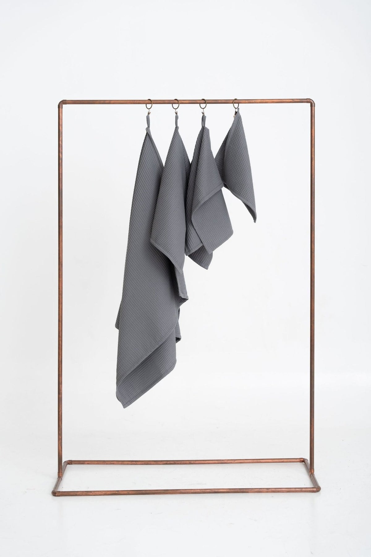 1. Set of four gray organic waffle cotton towels hanging on a copper rack against a white background