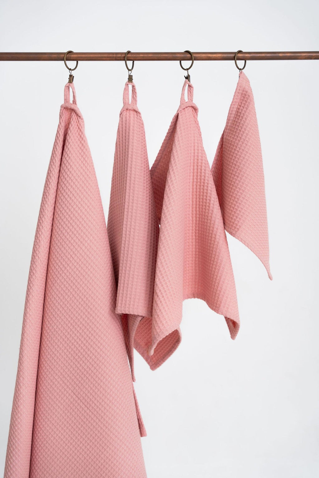 4. Four peach waffle cotton towels hanging on a rod, displaying various sizes and texture