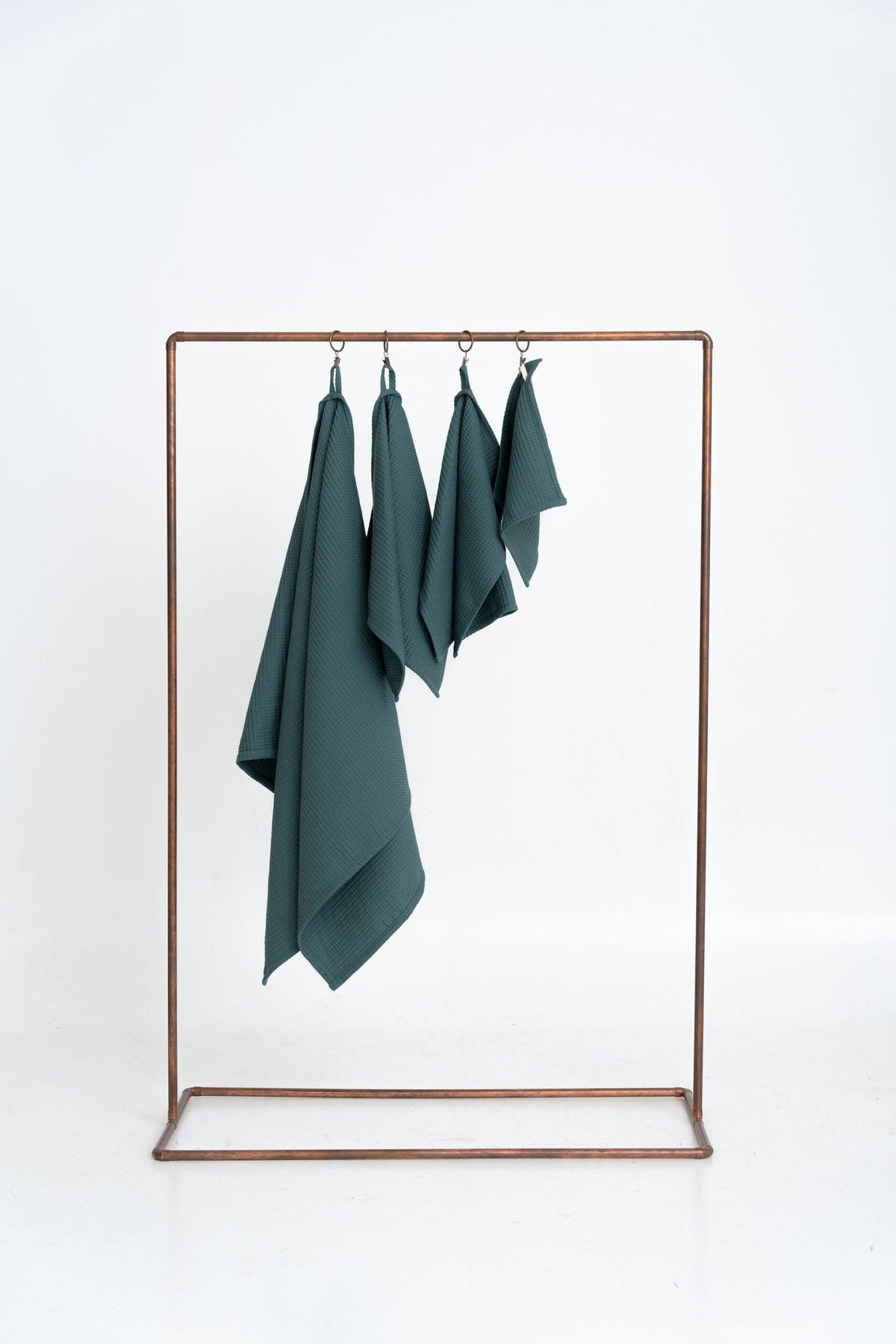 5. Size chart for petrol organic waffle cotton towels showing four sizes hanging on a copper rack