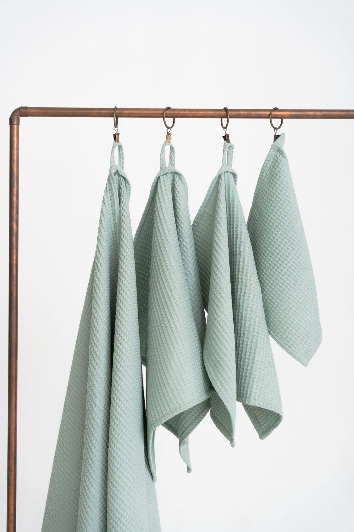 2. Studio shot of four sage green waffle cotton towels hanging on a metal rack