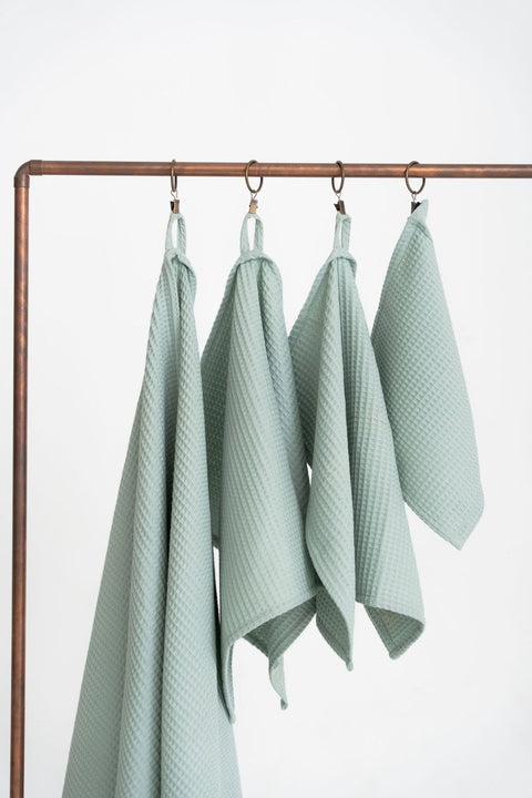 2. Studio shot of four sage green waffle cotton towels hanging on a metal rack