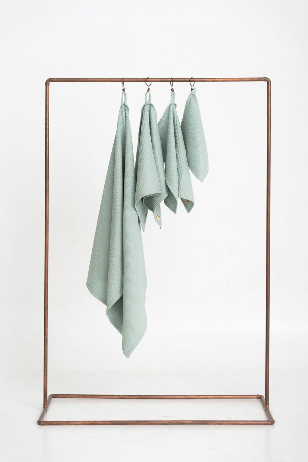 4. Flat lay of four sage green waffle cotton towels hanging on a metal rack