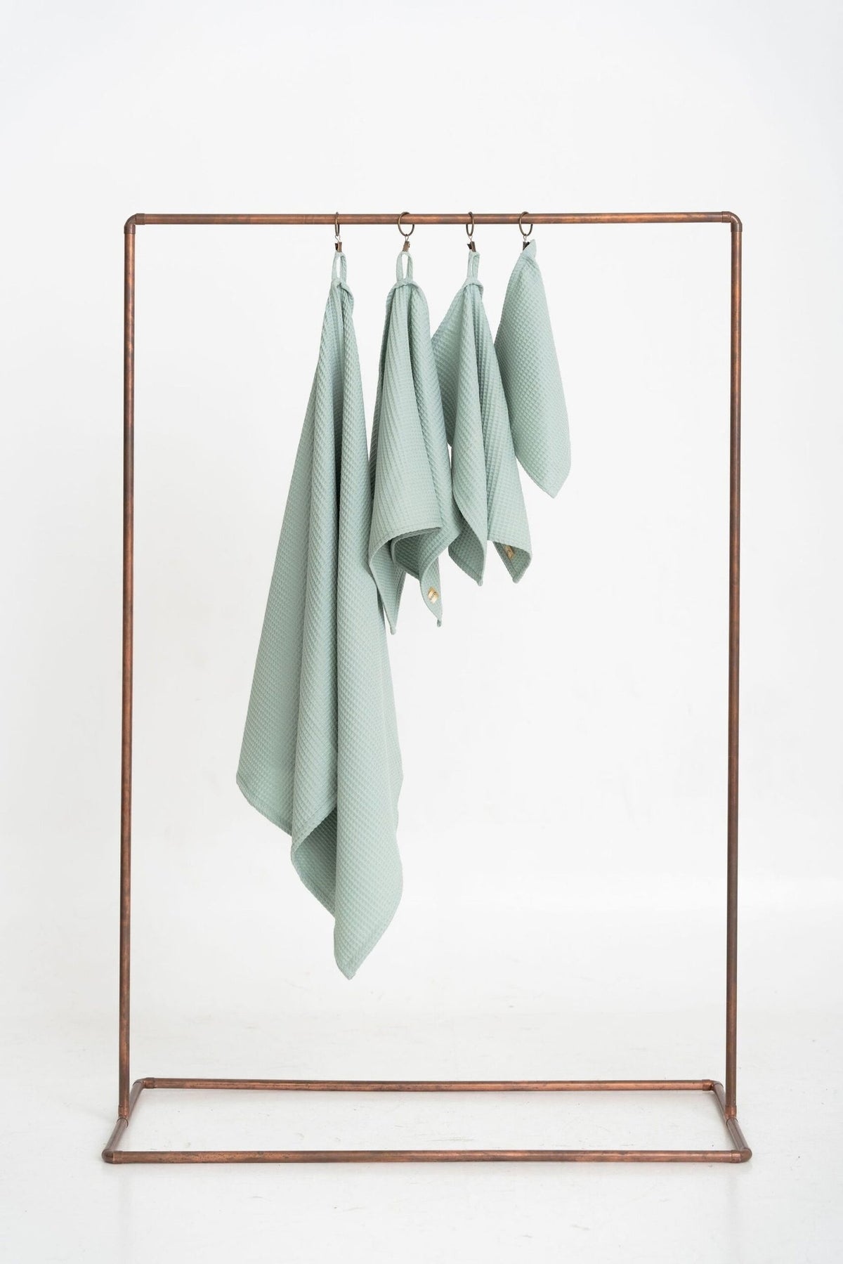 4. Flat lay of four sage green waffle cotton towels hanging on a metal rack