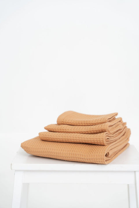 3. Stack of caramel waffle cotton towels in various sizes on a white stool, emphasizing texture and thickness
