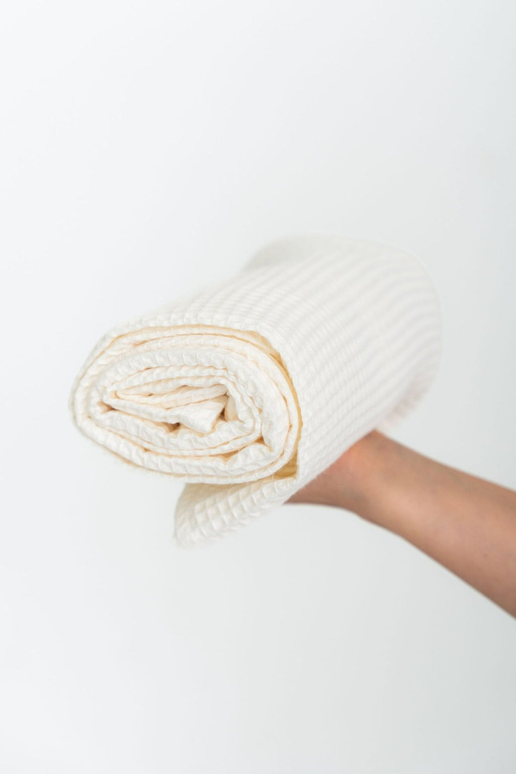 4. Rolled cream waffle cotton towel held in hand, showcasing texture and compact design