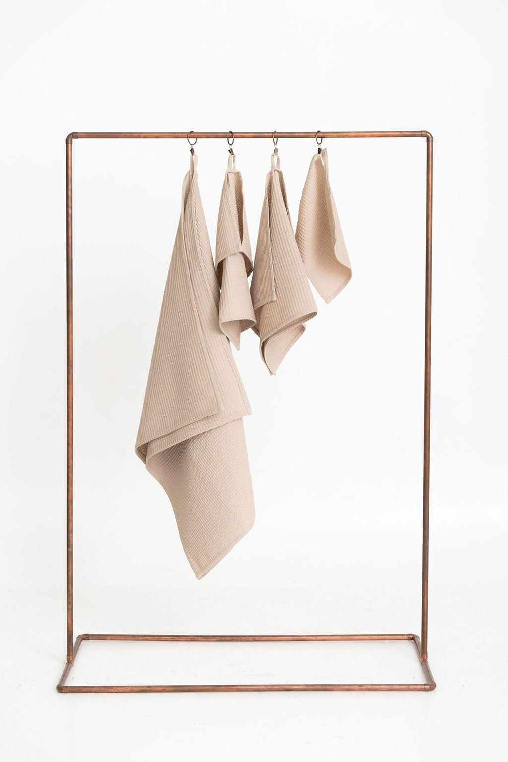 1. Set of four beige waffle cotton towels hanging on a metal rack, showcasing different sizes for versatile use in bathroom or kitchen