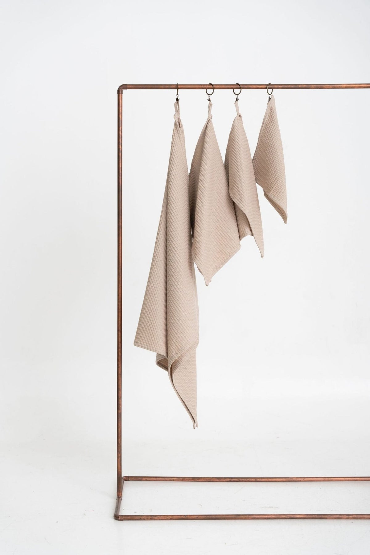 3. Beige waffle cotton towels in four sizes hanging on a minimalist metal rack, suitable for bathroom or kitchen