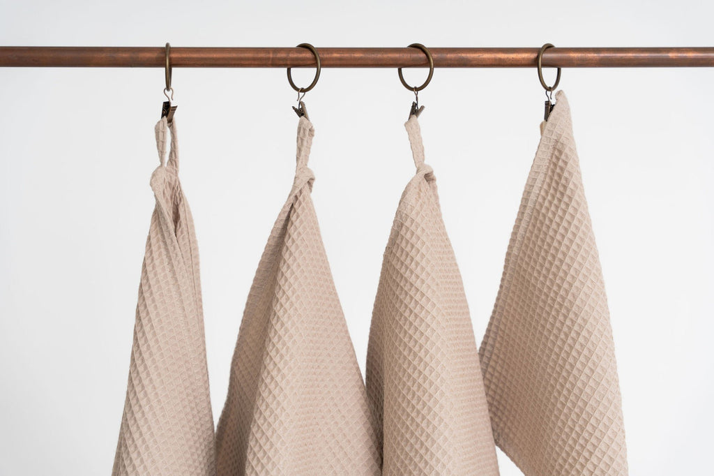 2. Close-up of four beige waffle cotton towels hanging from metal hooks, highlighting texture and hanging loops