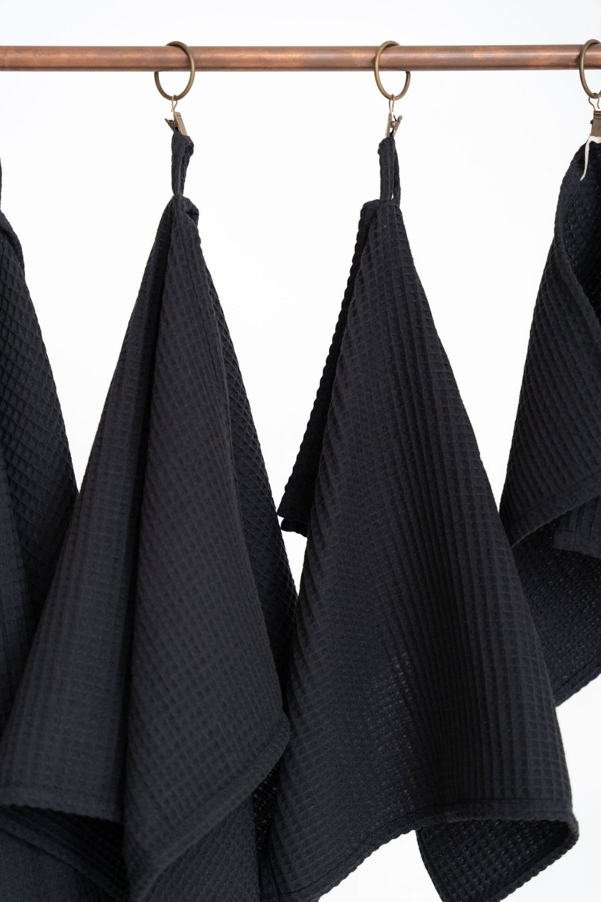3. Detail of black waffle cotton towels with visible texture and hanging loops on a copper rod