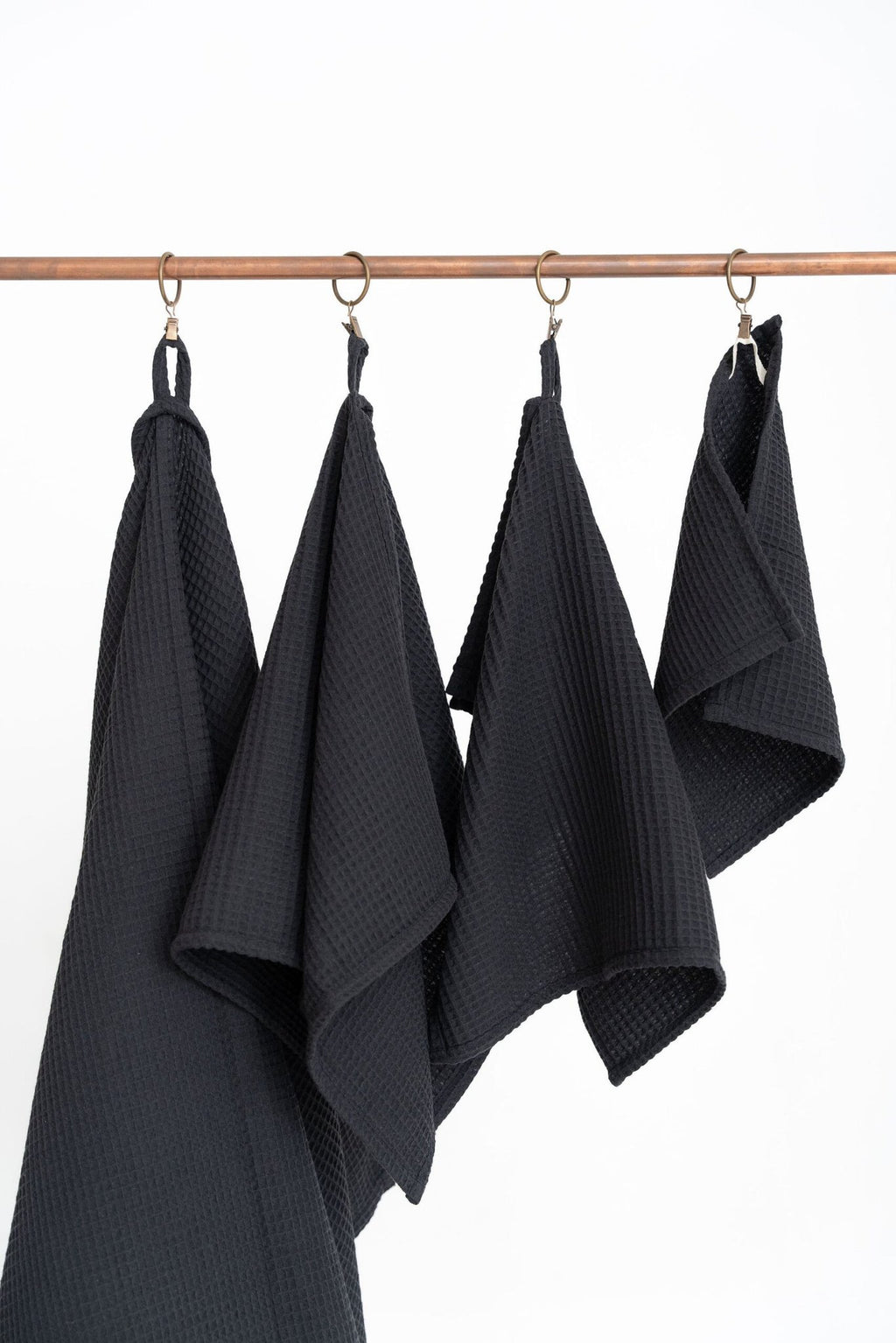 2. Close-up of four black waffle cotton towels hanging on a copper rod, showcasing texture and hanging loops
