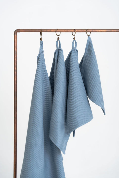 1. Set of four blue waffle cotton towels hanging on copper rod, showcasing different sizes with hanging loops