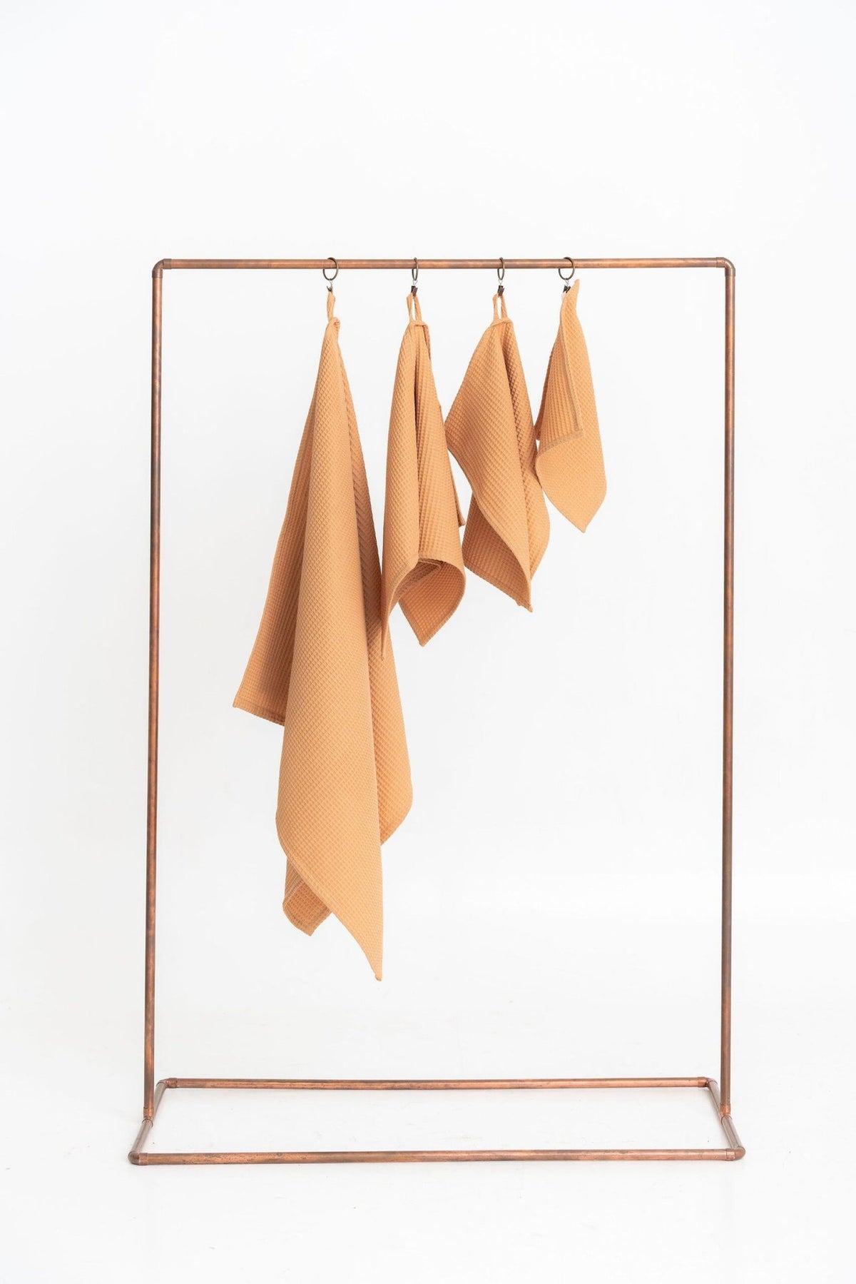 1. Set of four caramel waffle cotton towels hanging on a metal rack, showcasing different sizes with hanging loops, against a white background