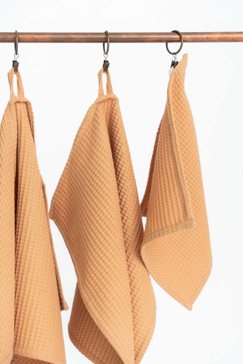 2. Close-up of caramel waffle cotton towels with hanging loops on a metal rod, highlighting texture and weave