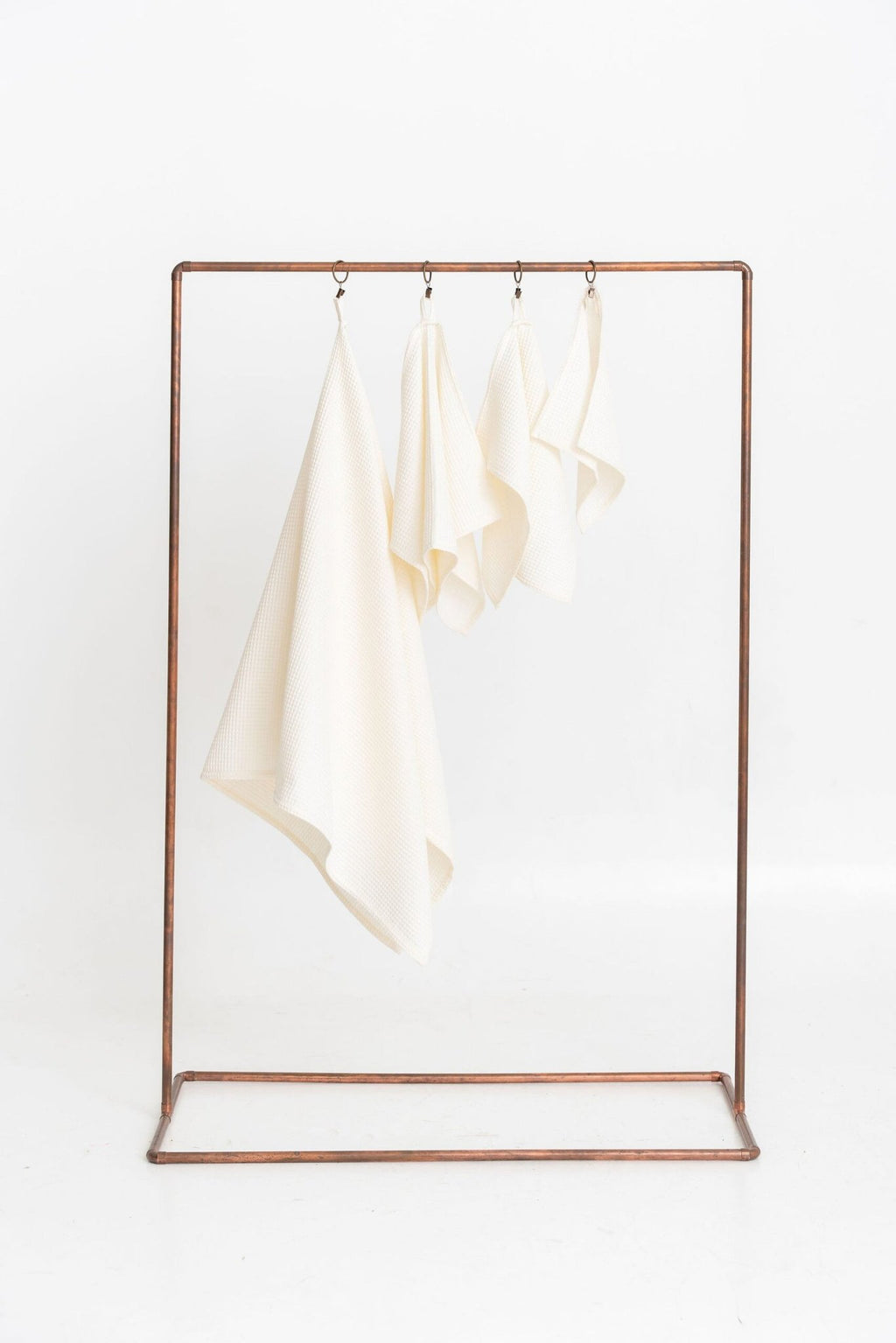 1. Set of four cream organic waffle cotton towels hanging on a metal rack, showcasing different sizes for versatile use
