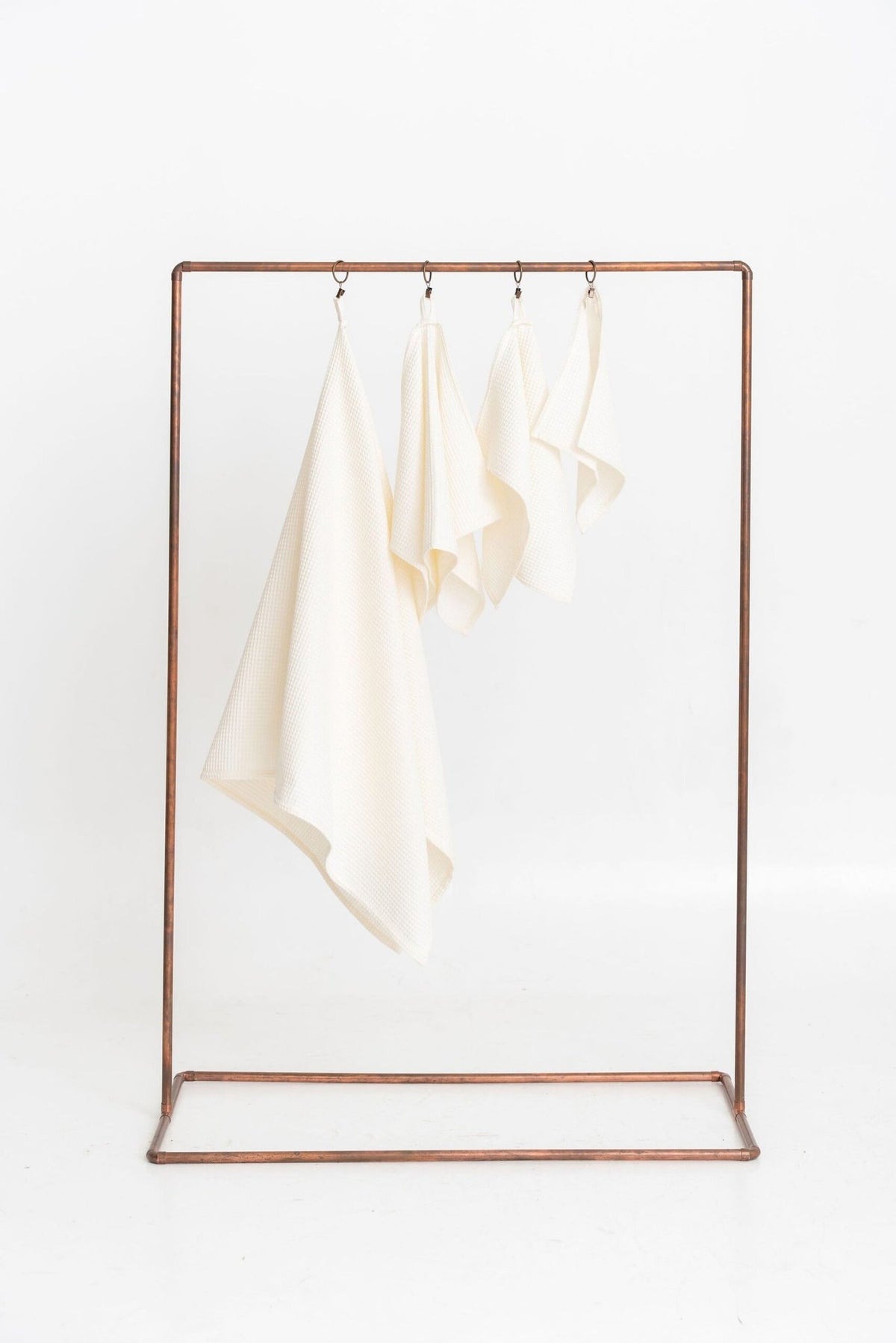 1. Set of four cream organic waffle cotton towels hanging on a metal rack, showcasing different sizes for versatile use