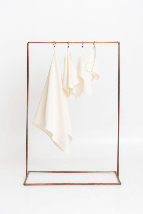 1. Set of four cream organic waffle cotton towels hanging on a metal rack, showcasing different sizes for versatile use