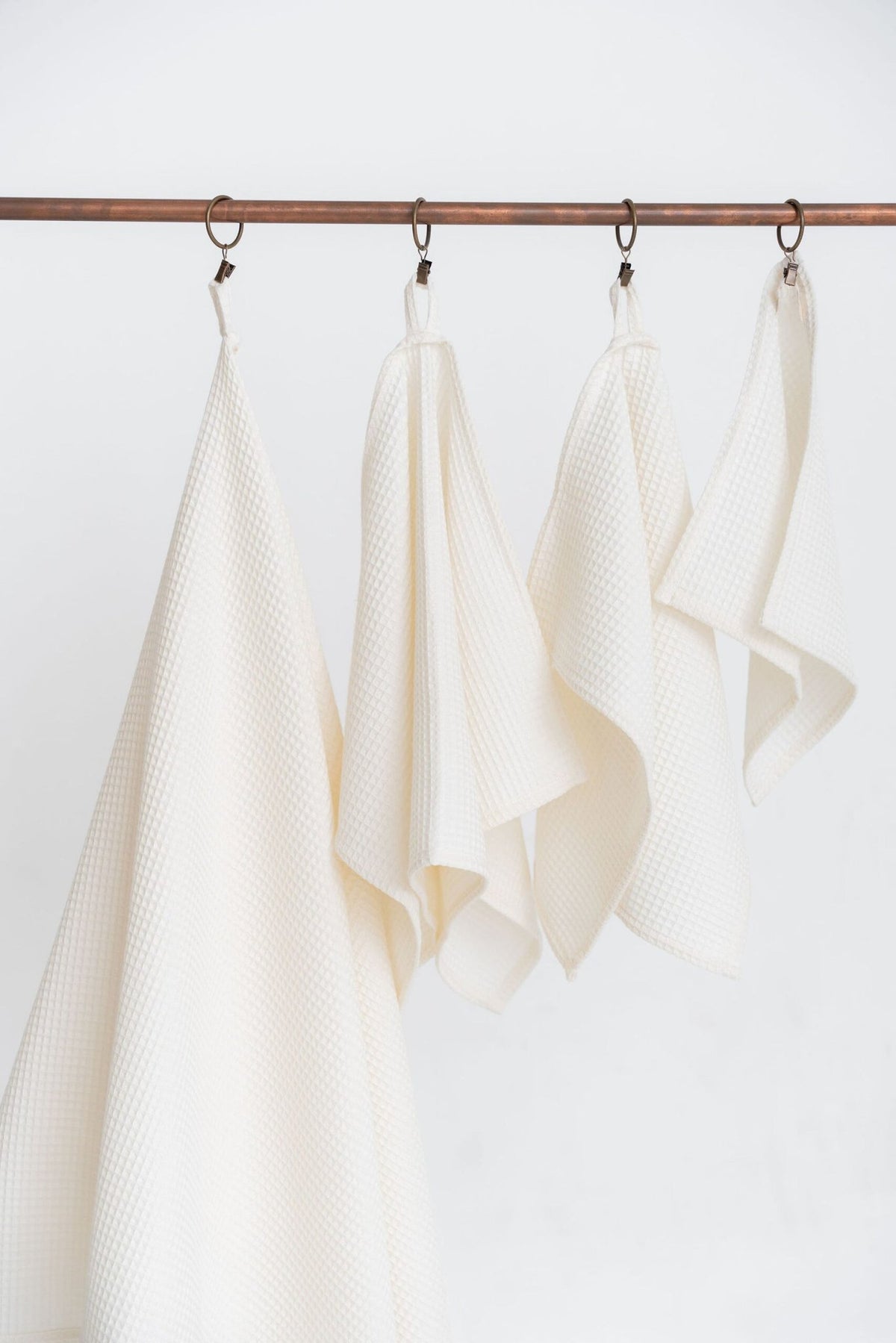 2. Cream waffle cotton towels in four sizes hanging on a metal rack, highlighting versatile design