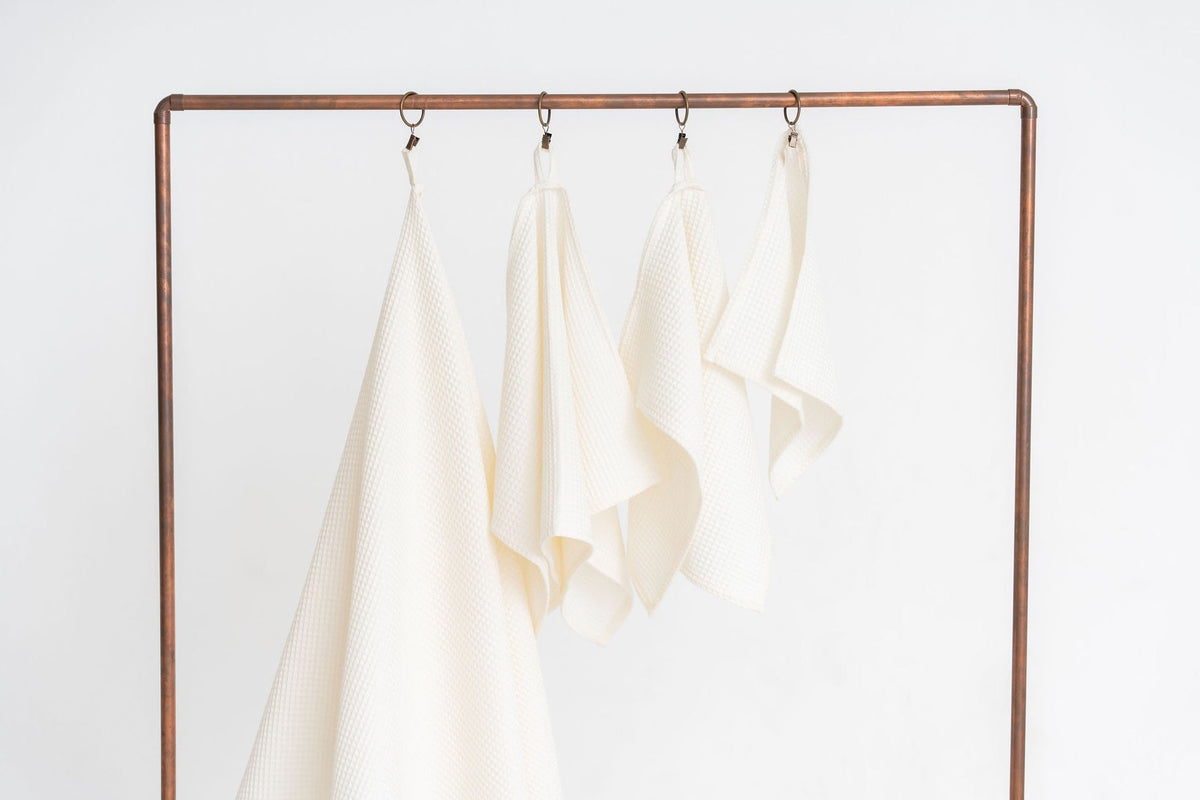 2. Four cream waffle cotton towels by Nuss hanging on a metal rack, showing various sizes