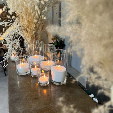 5. Multiple Candledust powder candles lit in various glass containers on a table with decorative plants