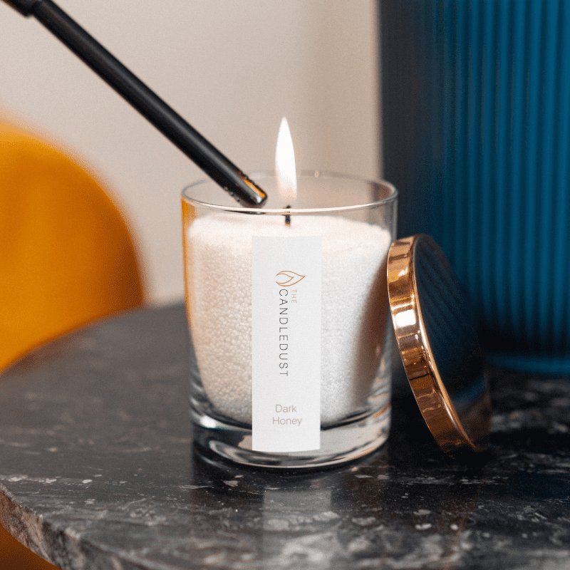 3. Close-up of Candledust Dark Honey powdered candle being lit, highlighting rose gold lid and clean-burning cotton wick