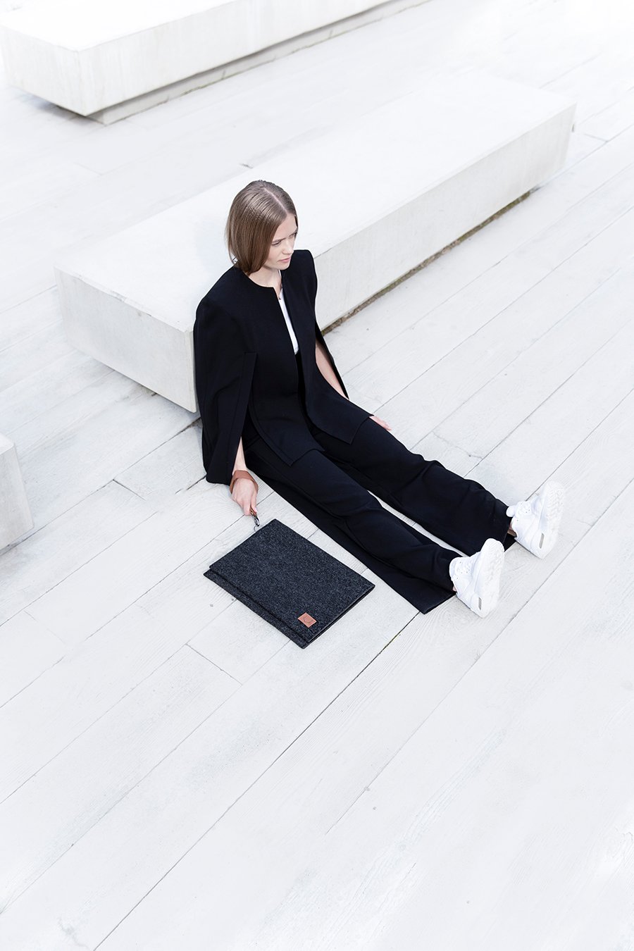 2. Woman sitting with Nordhale Berg 13'' grey laptop bag on white floor, showcasing minimalist design