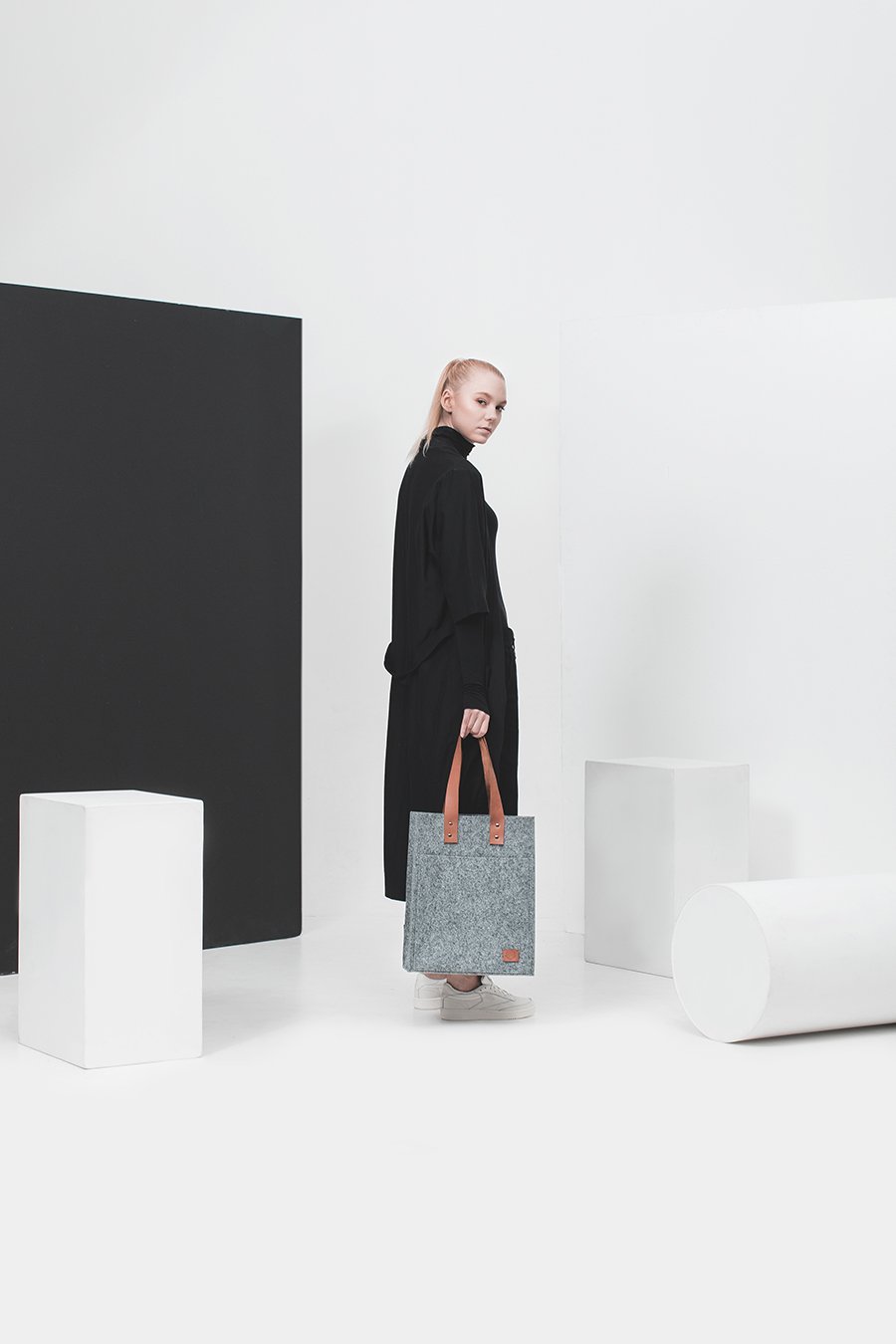 2. Woman in black dress holding Nordhale Hennes Tote Bag in grey, studio setting with modern decor