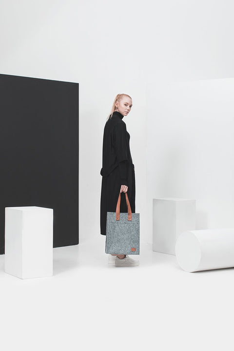 2. Woman in black dress holding Nordhale Hennes Tote Bag in grey, studio setting with modern decor