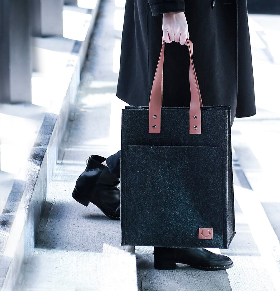 2. Unisex black Nordhale Hennes Tote Bag with brown leather handles, carried by a person in a black coat outdoors