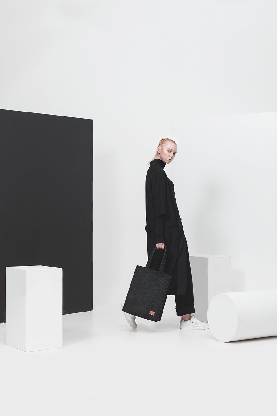 3. Woman in a studio setting holding Nordhale Hof Tote Bag in black, showcasing minimalist style