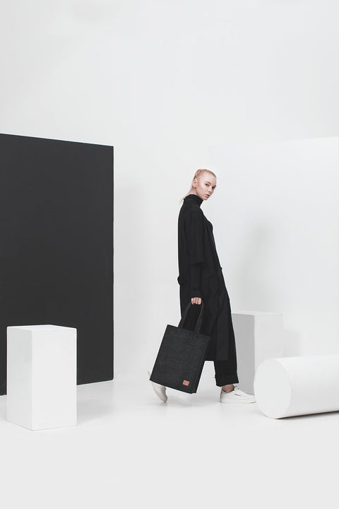3. Woman in a studio setting holding Nordhale Hof Tote Bag in black, showcasing minimalist style